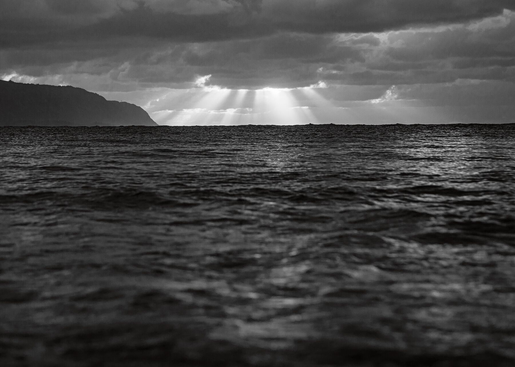 Sun rays break through the clouds over the ocean from the shores of Oahu, Hawaii