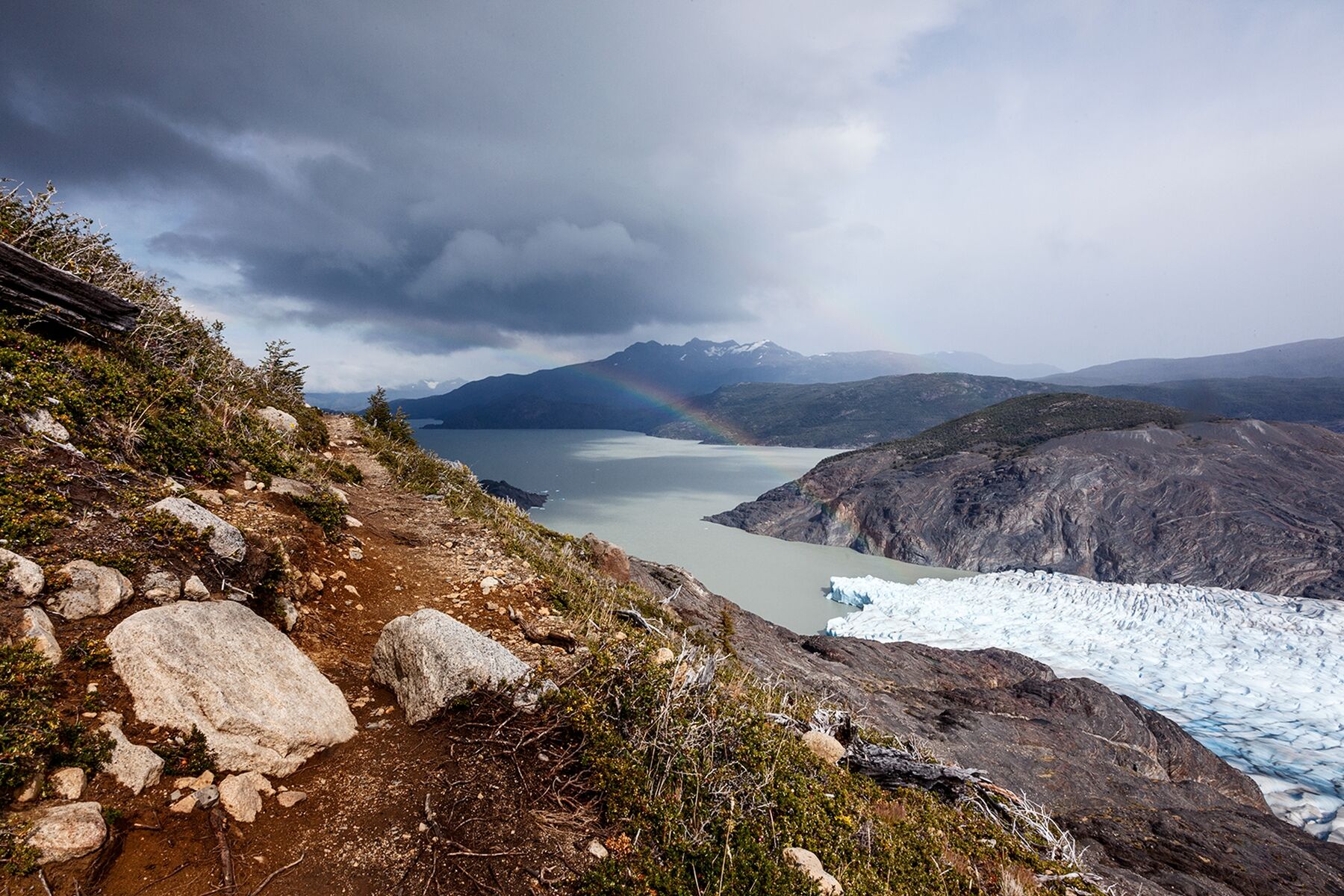 A rainbow breaks through the clouds and ends at the base of Glacier Gray in Torres Del Paine National Park, Chilean Patagonia