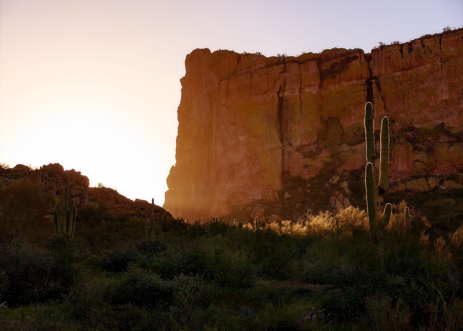 Sun peaks around a rock formation over a saguaro cactus in Lost Dutchman State Park, Arizona