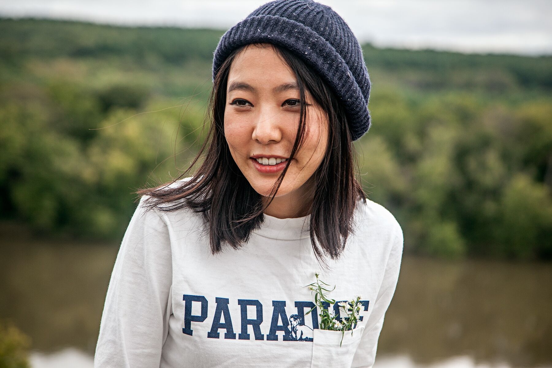 Soo wearing a hat posing in front of a river and trees