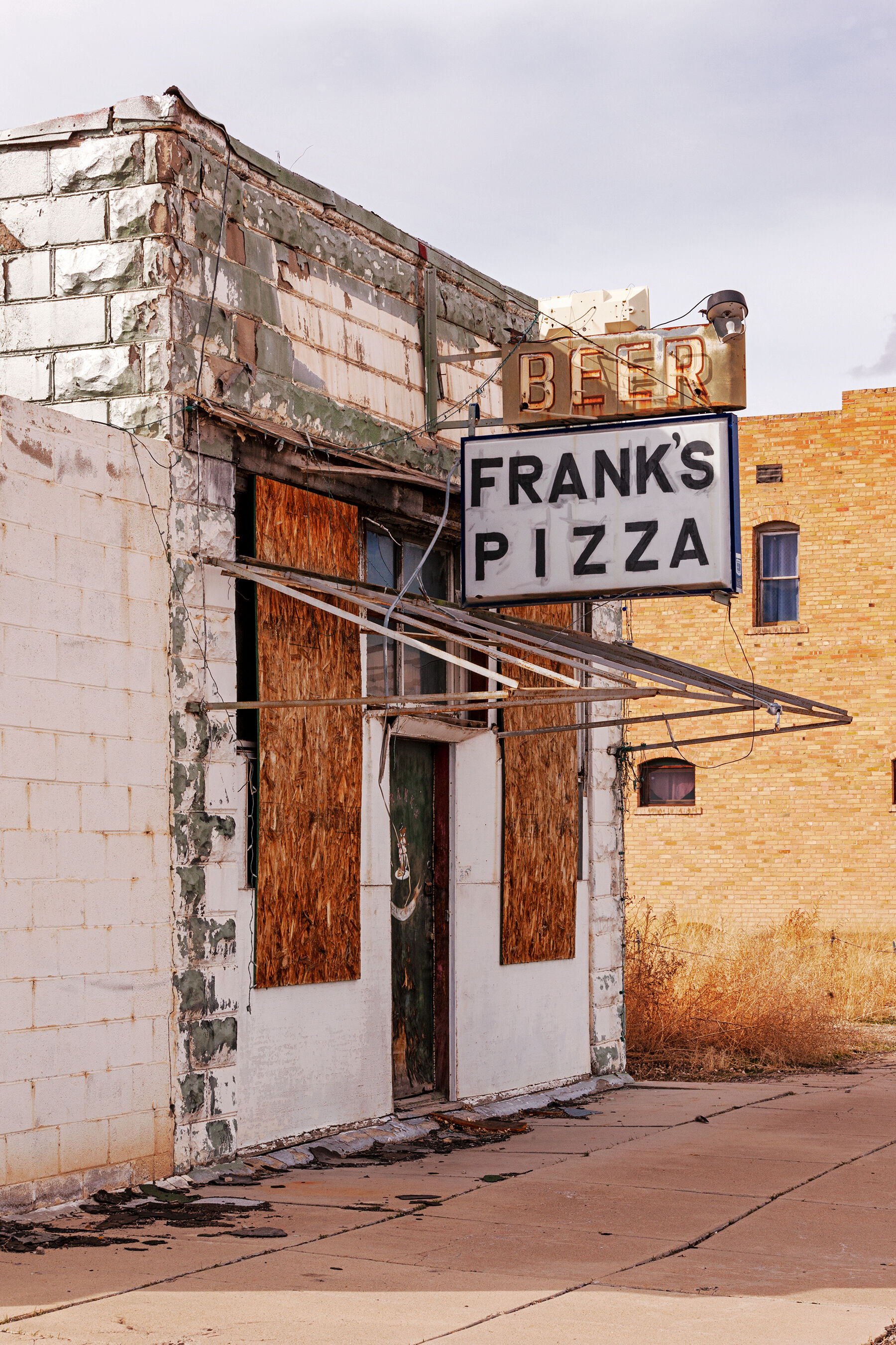 An old neon sign saying beer, franks pizza on an small white boarded up building in Green River, Utah